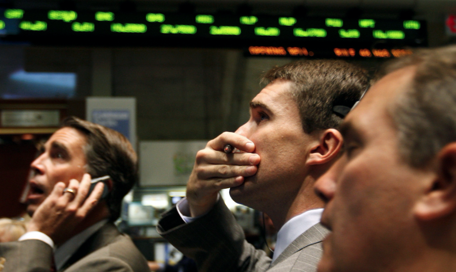 Photo of traders wearing suits and looking at screens with expressions of horror and disbelief, hands covering their mouths