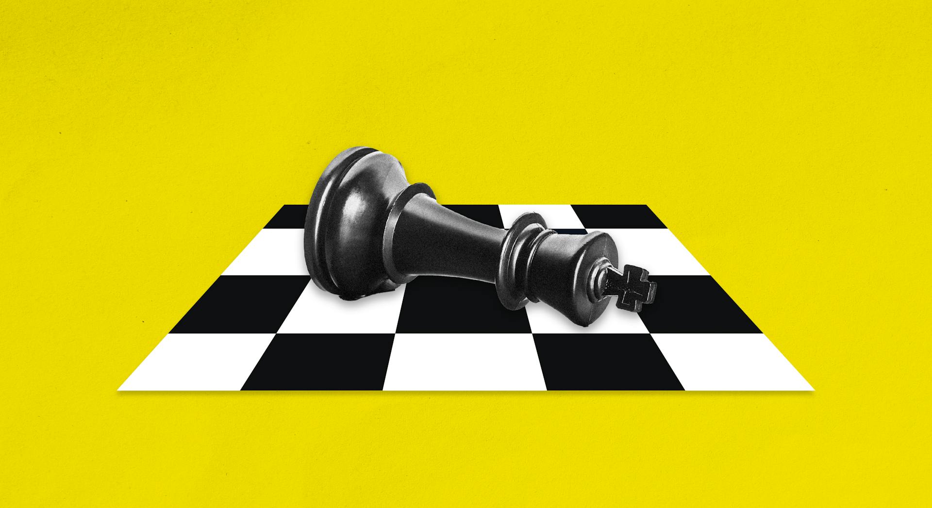 A chess piece is on its side on a chess board, on a yellow background. 