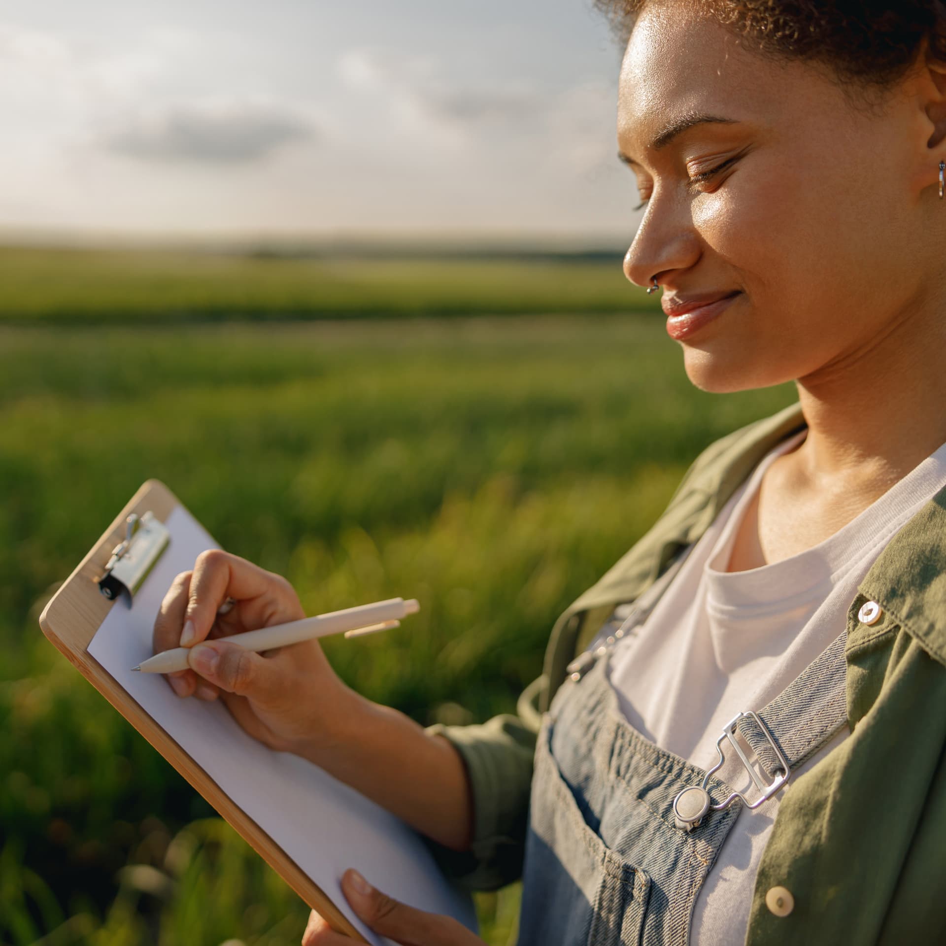 A woman in a sunny field writing notes on a clipboard A woman in a sunny field writing notes on a clipboard