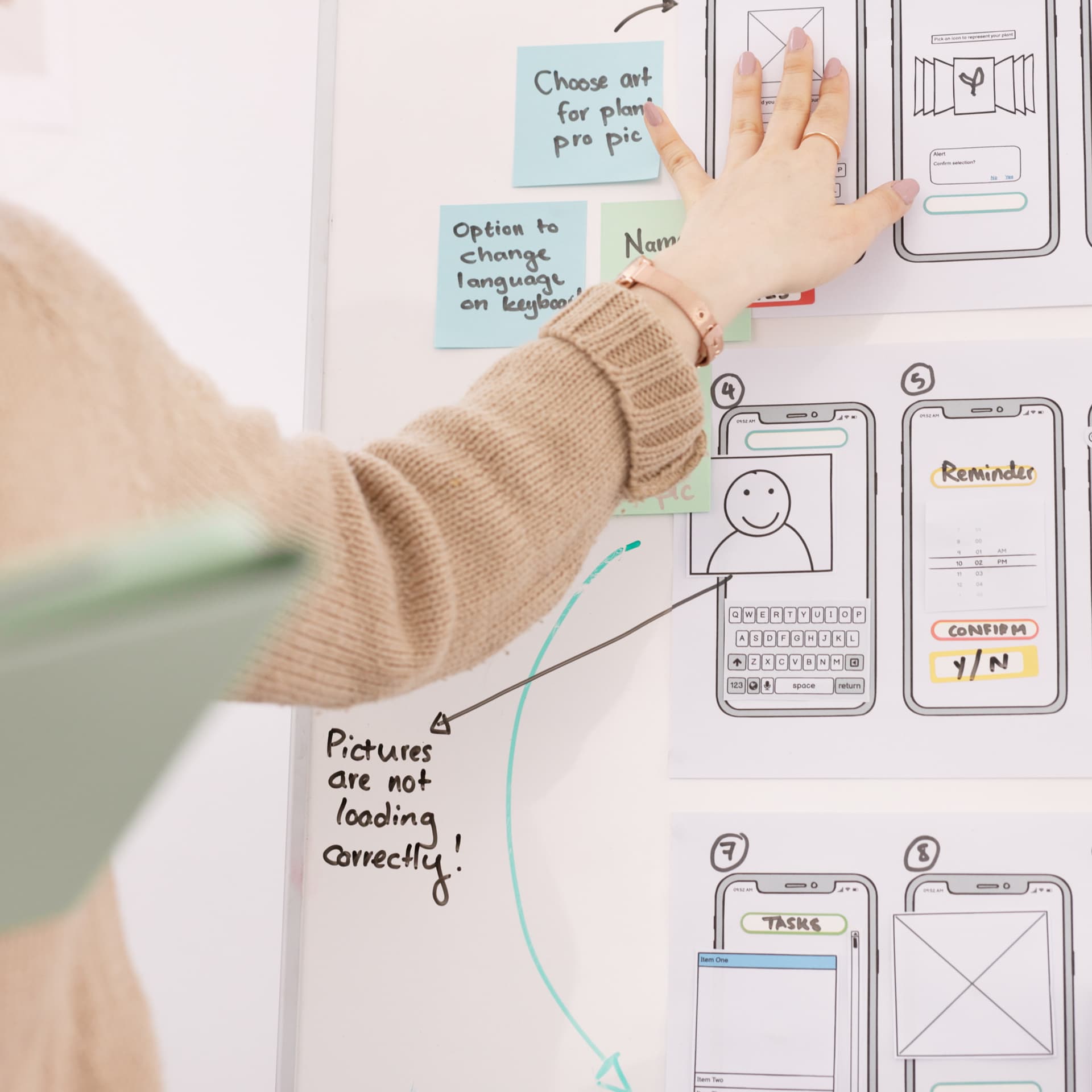 A person gesturing to wireframes pinned up on a board A person gesturing to wireframes pinned up on a board